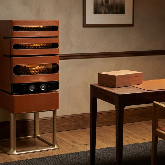 Afidano L3 Artistry cigar humidor cabinet on its gold stand beside a walnut desk holding a small cedar humidor box