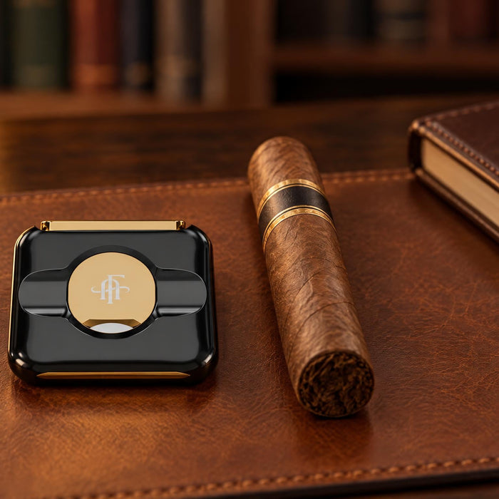 Afidano luxury stainless steel cigar cutter in black and gold on a leather desk blotter beside an unlit cigar