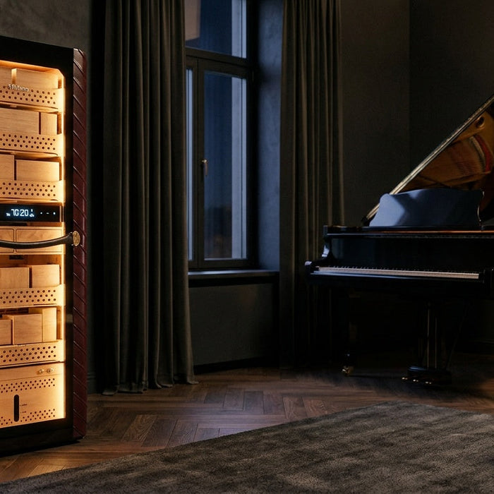 Afidano C8 Atelier electric cigar humidor beside a grand piano, lit Spanish cedar shelves behind its glass door
